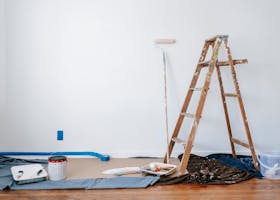 A room prepared for renovation with a ladder, paint supplies, and drop cloth.